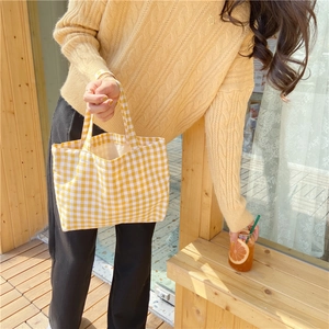 Detail of yellow plaid cotton linen tote bag held by a person in a sunny outdoor setting