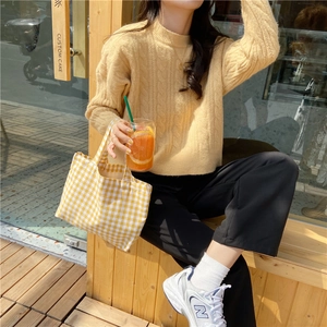 Close-up of loose-fitting beige knit sweater with classic cable pattern in outdoor setting