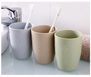 Close-up of three textured plastic rinse cups in grey beige and green with toothbrushes