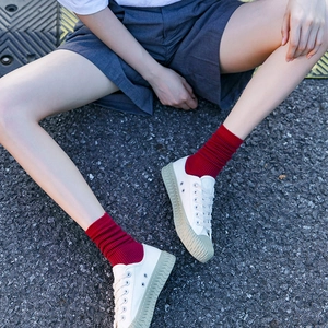 Women's bright red ribbed cotton mid-calf socks styled with white canvas shoes on asphalt