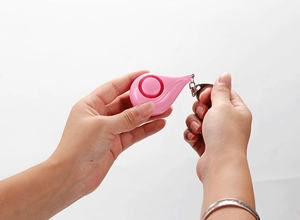 Pink teardrop personal alarm for women being operated by hands with keychain attachment