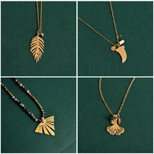 Macro detail of gold-plated feather, moon, and leaf charms on beaded necklaces