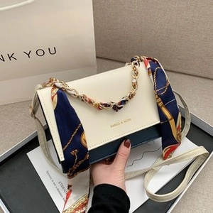 Detail of contrast flap handbag with gold chain strap wrapped in a floral silk scarf