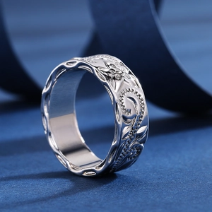 Polished silver ring with intricate floral vine carvings and wavy edges on blue silk