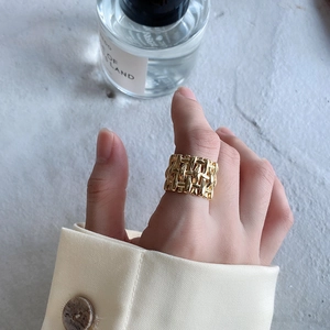 Close-up of a wide woven texture gold ring worn by a model in a luxury setting