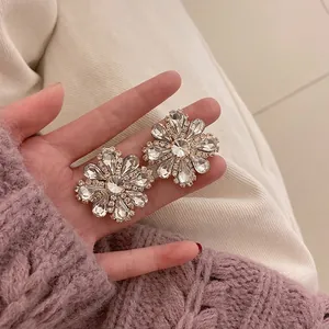 Sparkling oversized crystal sunflower earrings held against a cozy knit sweater background