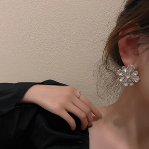 Close-up of sparkling crystal flower stud earrings and a thin ring on a female model