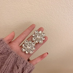 Macro shot of silver flower earrings with clear sparkling crystals held by hand