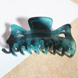 Detail of large teal gradient claw clip with hollow geometric design and spring mechanism