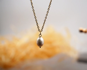 Close-up of a minimalist gold necklace with a teardrop-shaped white freshwater pearl