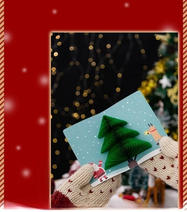 Detailed 3D pop-up Christmas tree card with festive illustrations held in gloved hands