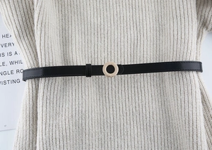 Detail of slim black leather belt with golden circle buckle on white knit dress