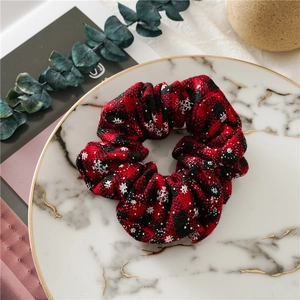 Detail of red and black plaid Christmas scrunchie with white snowflakes on marble tray
