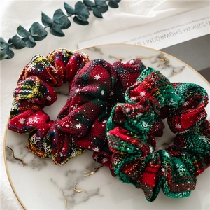 Close-up of red and green plaid Christmas scrunchies with snowflake patterns on marble tray