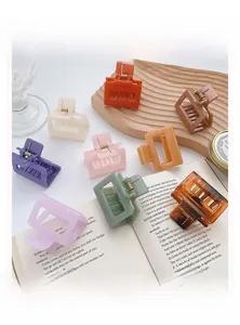 Close-up of nine assorted matte acrylic hair claw clips on a wooden tray with a book