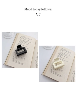 Minimalist square hollow hair claw clips in matte black and cream on an open book