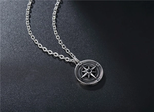 Detailed macro view of retro silver compass pendant with black bead on dark textured background