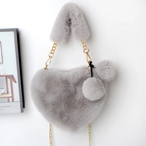 Detail of grey heart-shaped faux fur bag with golden chain and plush pompom charms