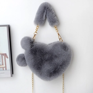 Detail of grey heart-shaped faux fur bag with golden chain strap and plush pom-poms