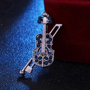 Vue macro d'une broche violon argentée avec strass bleus à côté d'un écrin rouge