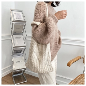 Detalle del bolso de punto beige con textura tejida sostenido por una modelo