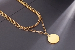 Close-up of golden double-layer chain necklace featuring flat round pendant on dark surface