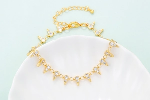 Detail of gold chain bracelet featuring pave zircon triangle charms on white shell decor