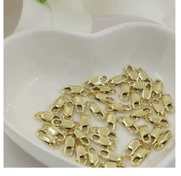 Macro detail of 14K gold plated lobster clasps in a white heart ceramic bowl