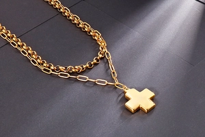 Macro detail of gold layered double chain necklace with a minimalist cross pendant
