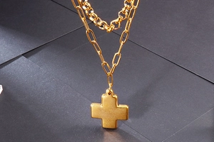 Close-up of gold double-layer necklace with mirror finish cross pendant on dark surface