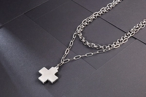 Detail of double-layer stainless steel necklace featuring a matte cross pendant