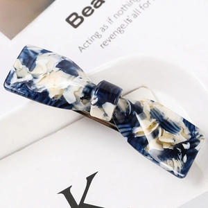 Detail of blue and beige marble acetate bow hair claw clip on a minimalist background