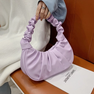 Light purple pleated shoulder bag with ruched handle shown on a brown leather bench