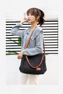 Detail of black canvas tote bag featuring brown leather handles and a side zipper pocket