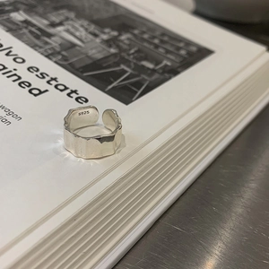 Irregular silver S925 wavy band ring with adjustable open design on a book