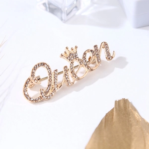 Gros plan de la broche dorée Queen avec strass sur un fond blanc minimaliste