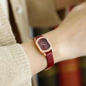 Close-up of elegant burgundy leather strap and rose gold tonneau watch on a female wrist