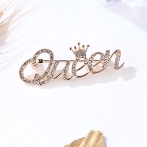 Détail de la broche Queen dorée avec strass scintillants et motif de petite couronne