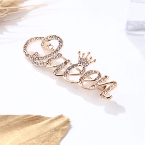 Détail d'une broche Queen dorée avec strass et couronne sur un décor blanc élégant