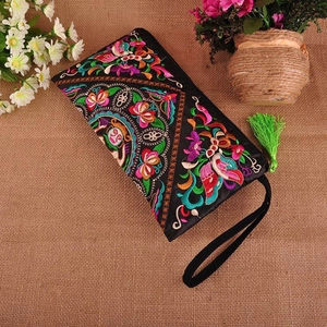 Close-up of black ethnic embroidered clutch bag with colorful floral patterns and green tassel