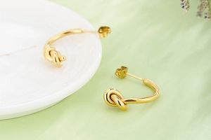 Détail de boucles d'oreilles nœud dorées avec finition polie et design incurvé en forme de C