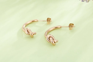 Détail des boucles d'oreilles créoles nouées en or rose avec texture métal poli