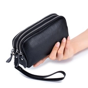 Macro shot of a black genuine leather clutch with three zippers and a wrist strap held by hand