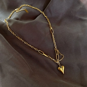 Détail du collier cœur doré avec chaîne asymétrique sur un tissu en soie
