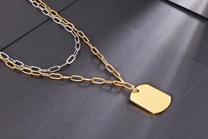 Detail of layered gold chunky chain and silver thin necklace with polished army tag pendant