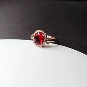 Detailed close-up of rose gold ring featuring a red ruby-style oval gemstone and halo diamonds