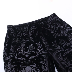 Close-up of black velvet flare pants featuring gothic floral embossed patterns and elastic waist