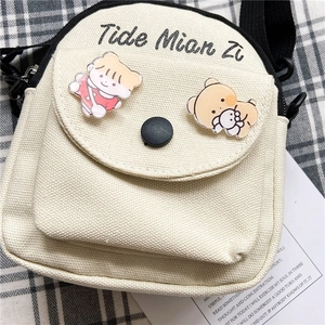 Detail of off-white canvas crossbody bag with cute cartoon pins and black artistic text