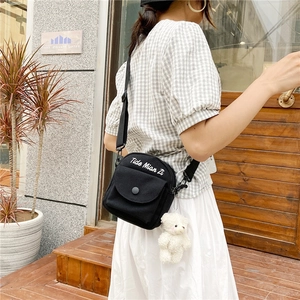 Detail of black canvas crossbody bag featuring white text and a cute plush bear charm