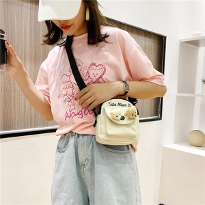 Detail of cream canvas crossbody bag featuring two plush bear ornaments and adjustable strap
